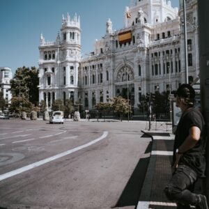 Man leans on pole in front of grand building.
